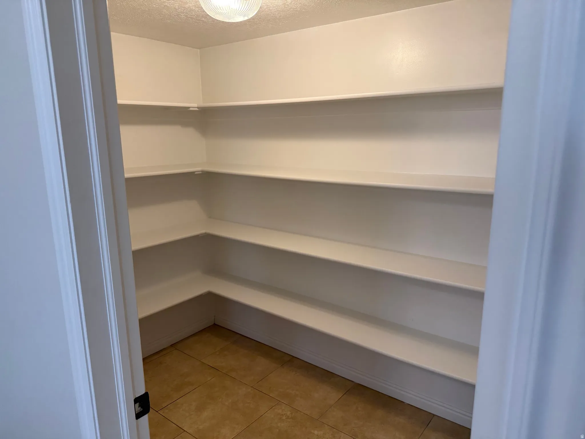 Spacious second pantry featuring extensive wrap-around shelving, tile flooring, and a flush-mount ceiling light fixture