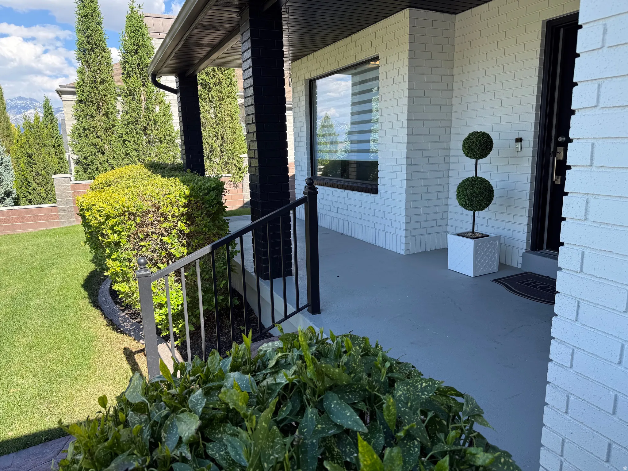 Welcoming front porch featuring white brick siding, dark contrasting trim, and a black metal handrail