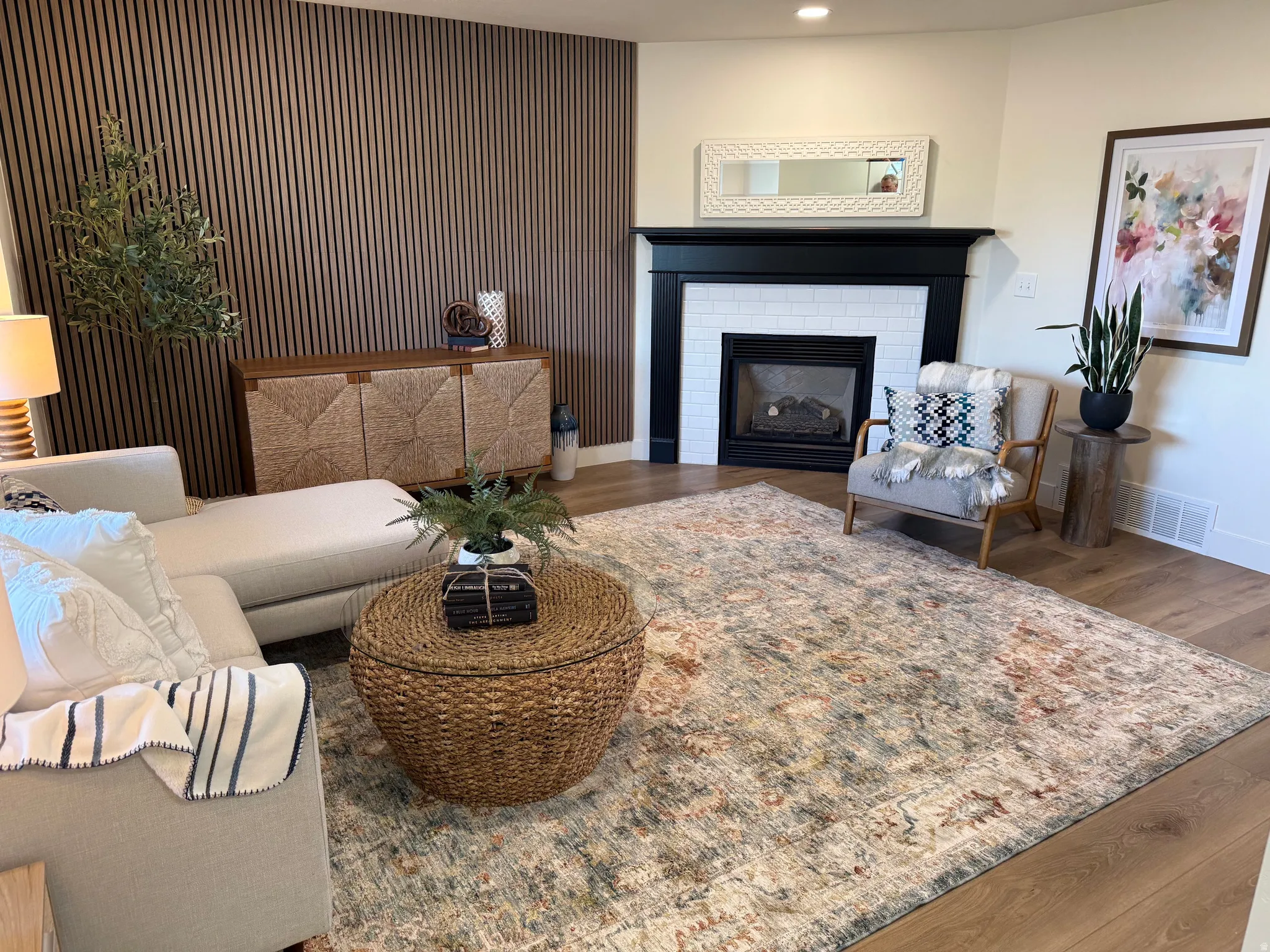Living area featuring a modern wood-slat accent wall, wood-finish flooring, a fireplace with a black mantel and white tile surround, and recessed lighting