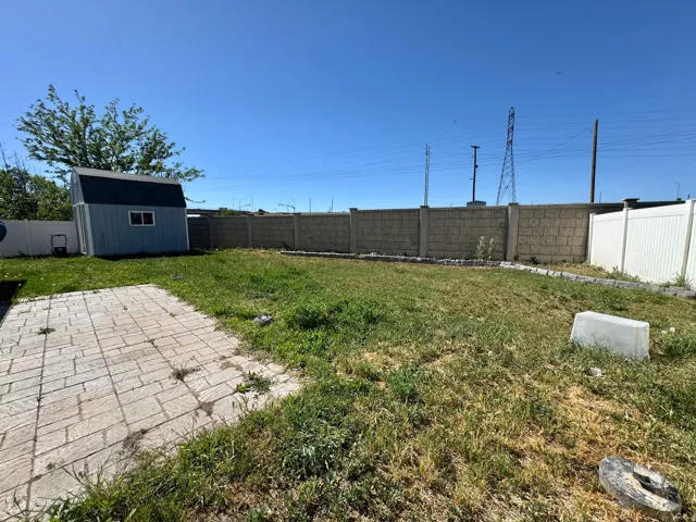 Expansive backyard featuring a stone paver patio, a light blue storage shed with white trim, and a combination of block and privacy fencing