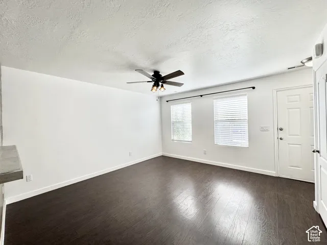 Spacious room featuring wood-finish flooring, white walls, two windows with blinds, and a ceiling fan with integrated lighting