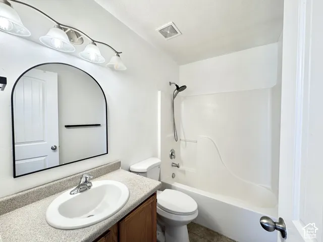 Vanity with laminate countertop and integrated sink, arched mirror, wall-mounted light fixture, and shower/tub combination with a showerhead and faucet