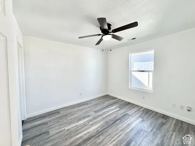White walls with wood-finish flooring, a window with a white frame, and a ceiling fan with integrated lighting