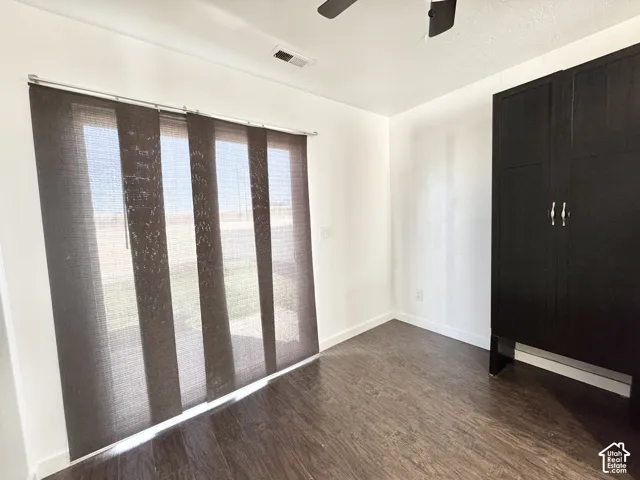 Dark wood-finish flooring with white baseboards, a built-in dark wood storage cabinet, and large panel track blinds
