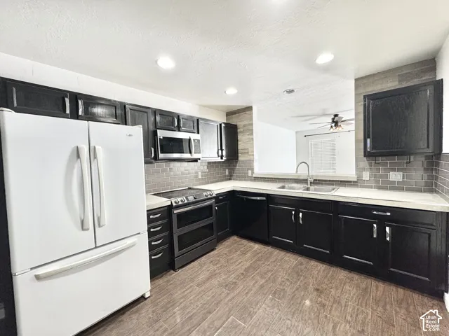 Kitchen featuring dark wood-finish cabinetry, stainless steel appliances, light countertops, and a gray tile backsplash