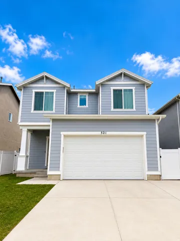 Two-story residence featuring light blue siding, white trim, a double-car garage, concrete driveway, and a fenced yard