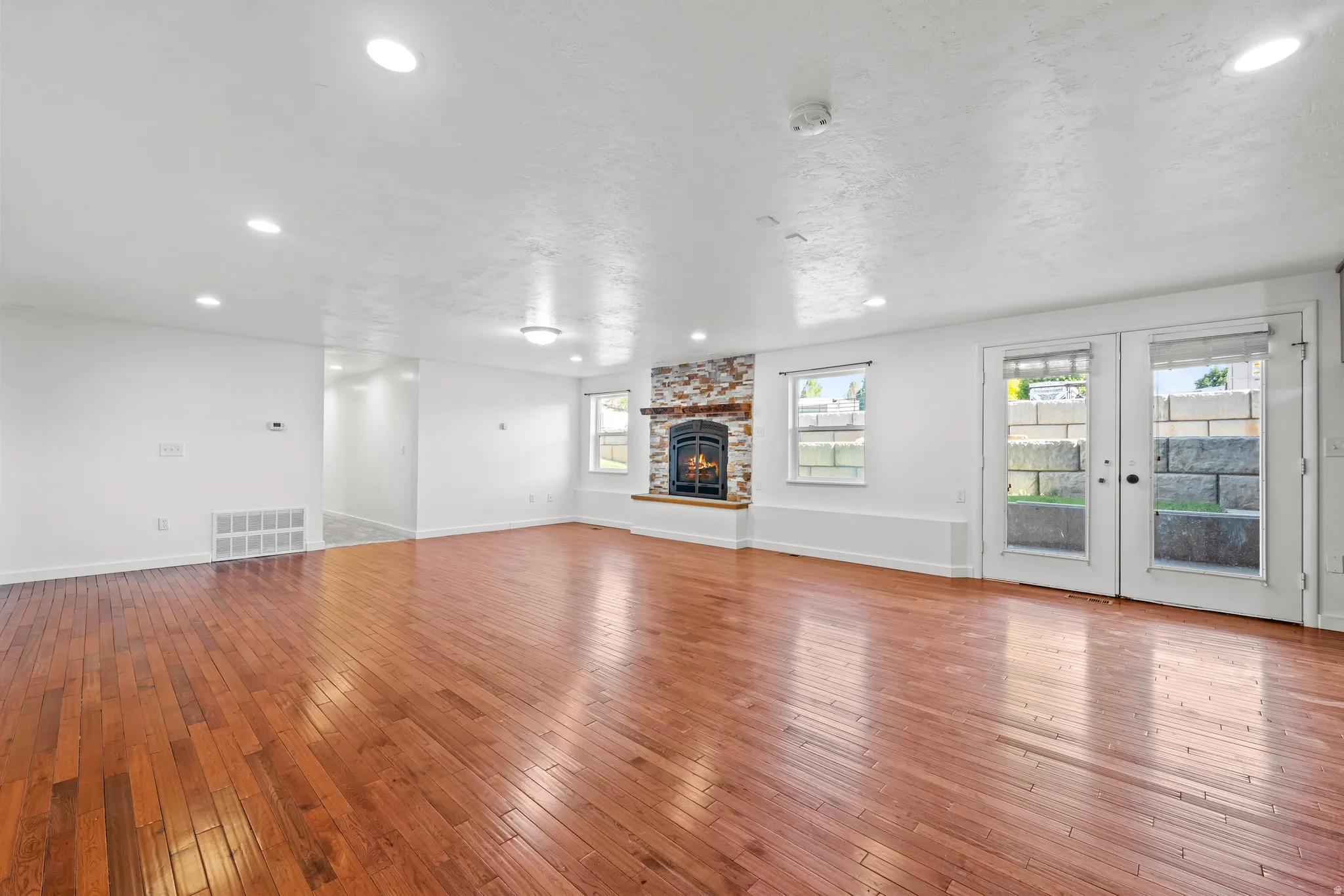 Spacious living area featuring wood-finish flooring, a stone fireplace, recessed lighting, and dual French doors