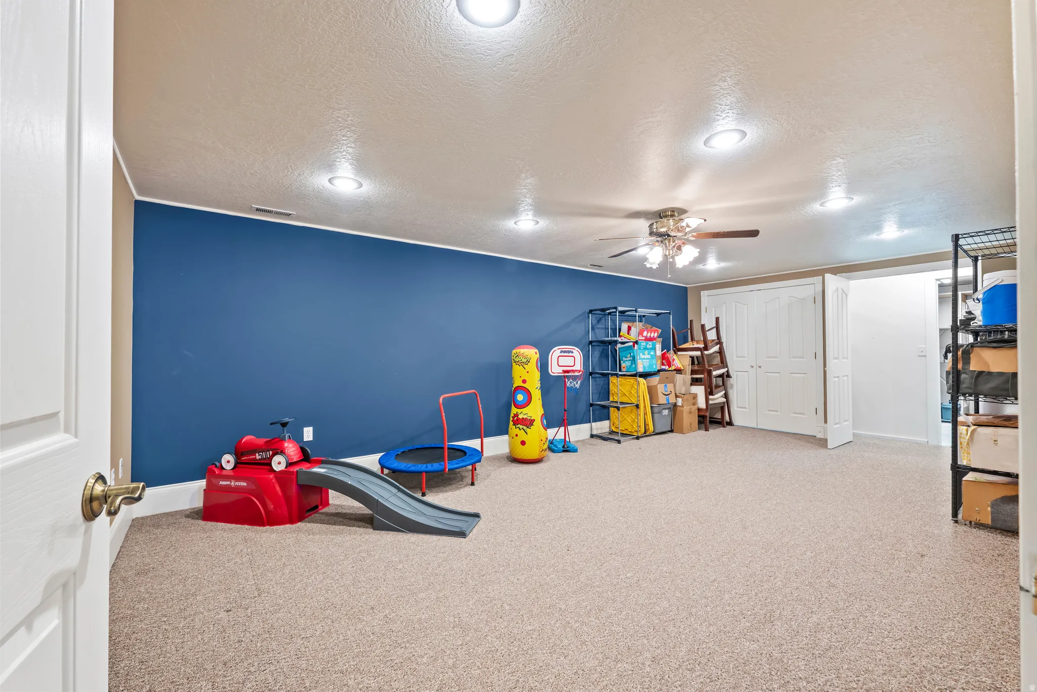 Expansive carpeted room featuring a ceiling fan with integrated lighting, recessed ceiling lights, and a blue accent wall