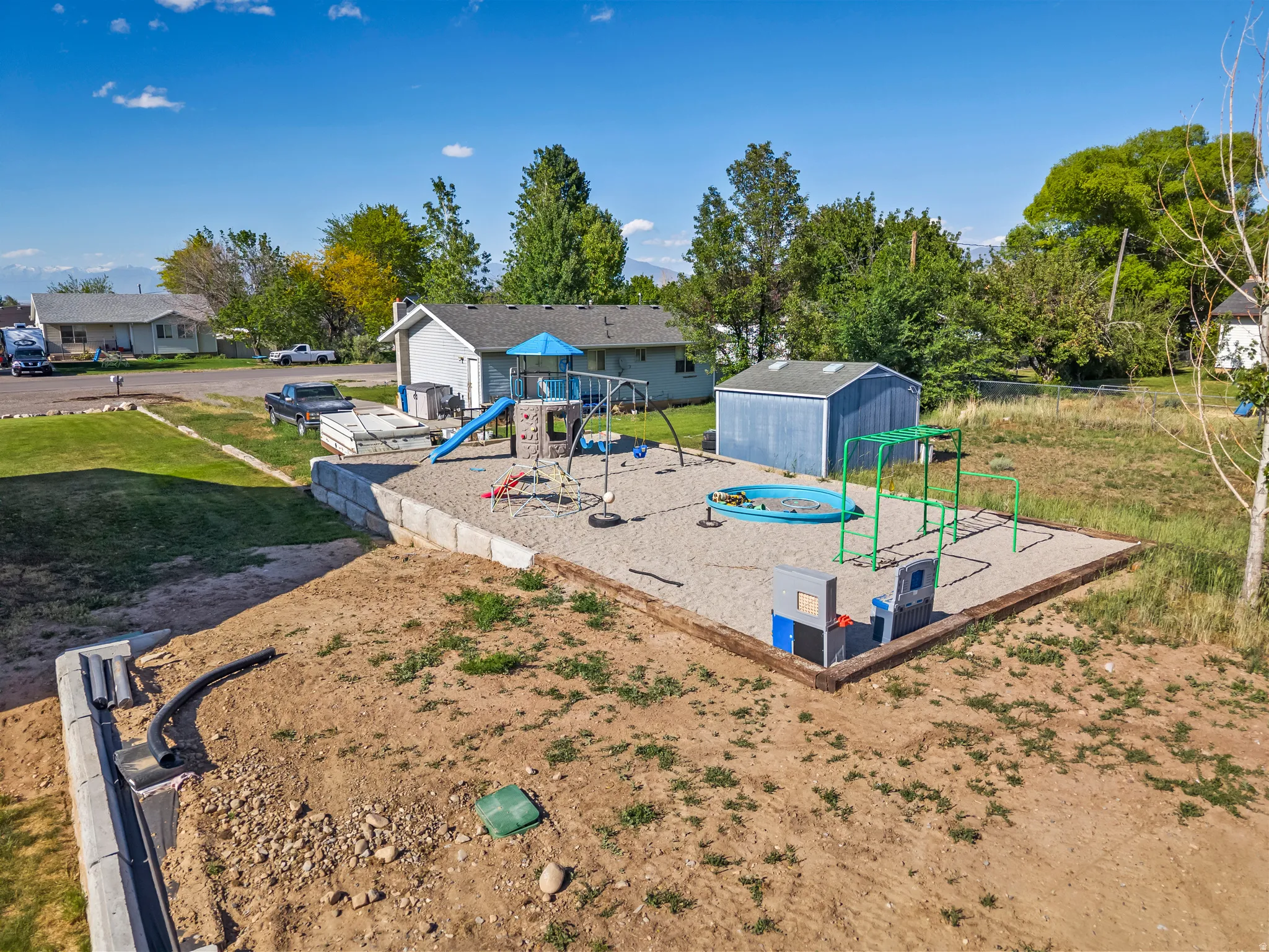 Outdoor play area featuring a sand base, a blue slide, a swing set, and a small blue wading pool