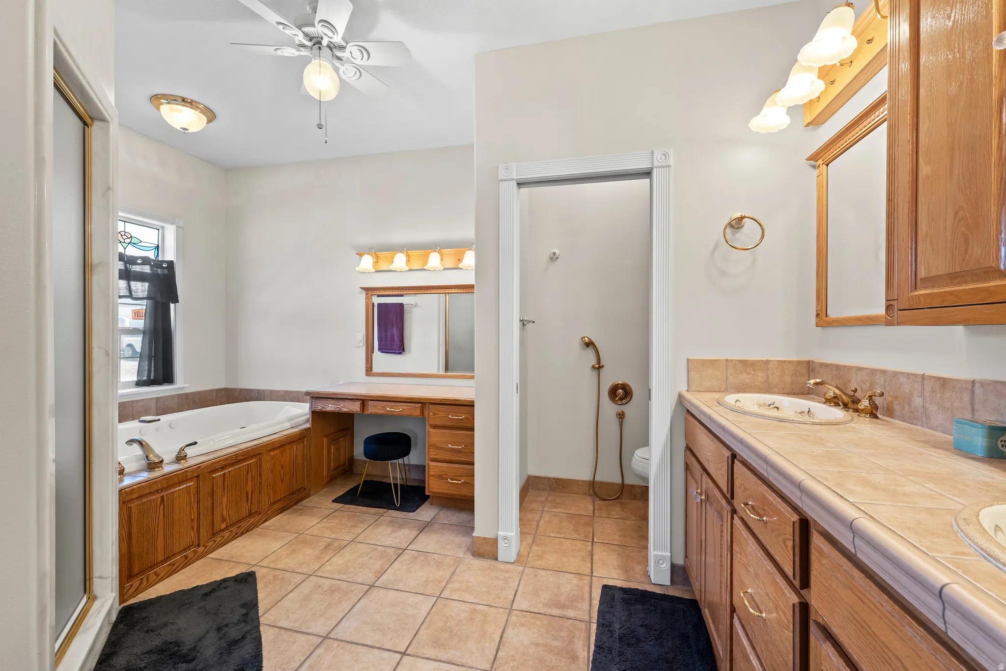 Spacious bathroom featuring a built-in jetted tub, wood-finish cabinetry, tile flooring, dual vanity with undermount sinks, and a separate shower enclosure