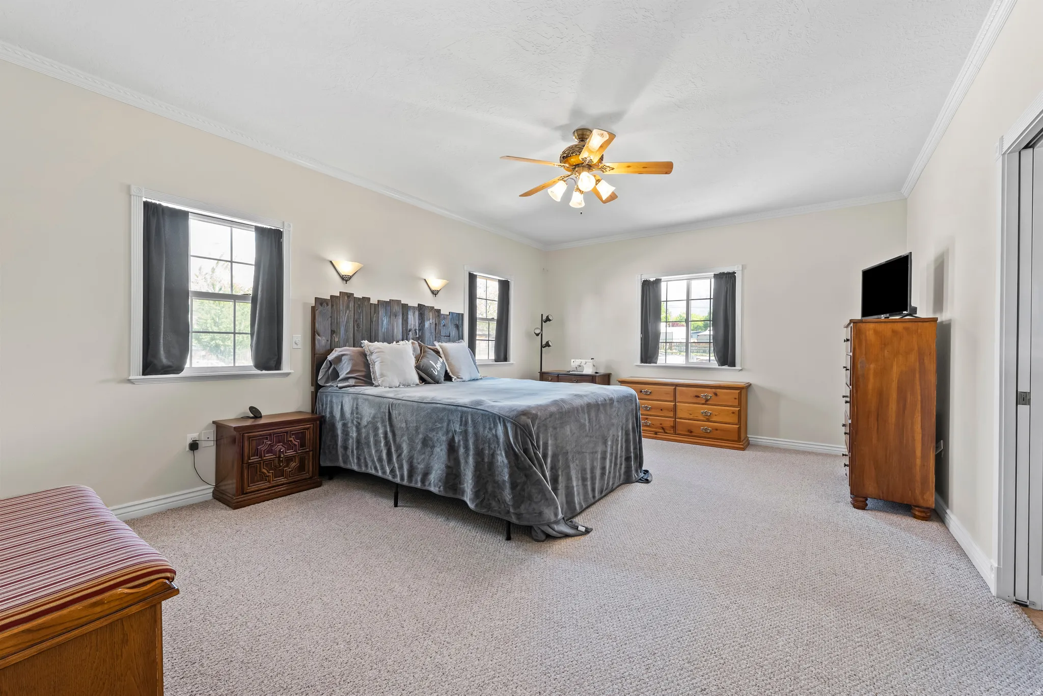 Spacious room featuring neutral carpeting, a ceiling fan, crown molding, and multiple windows