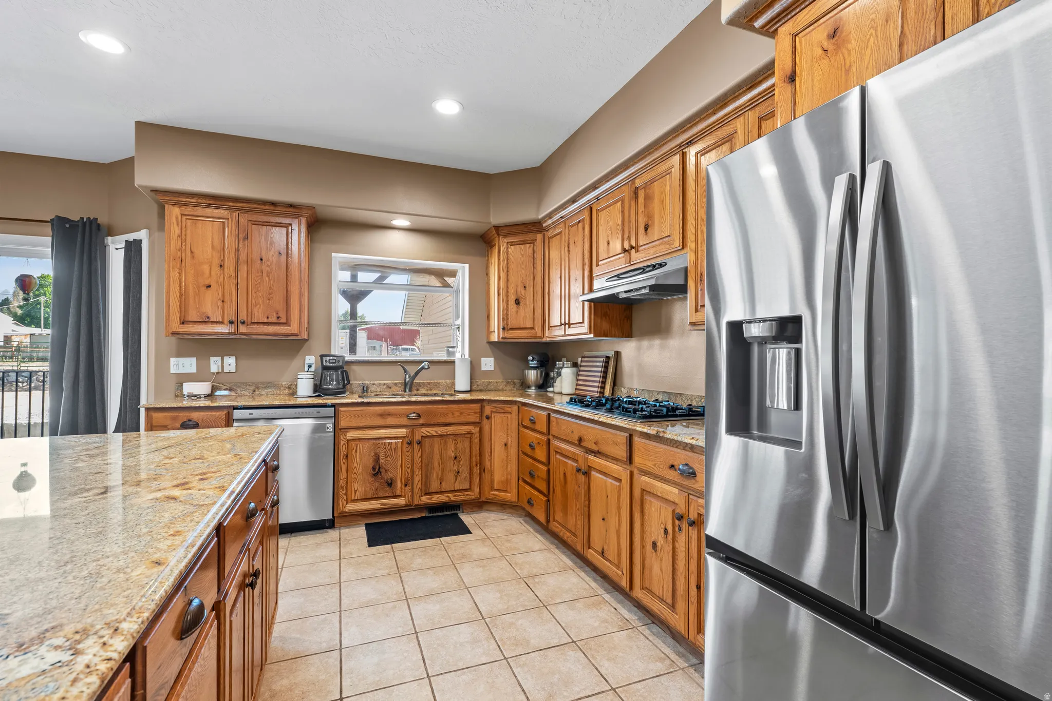 Kitchen featuring wood cabinetry, granite countertops, tile flooring, and stainless steel appliances including a refrigerator, dishwasher, and gas range