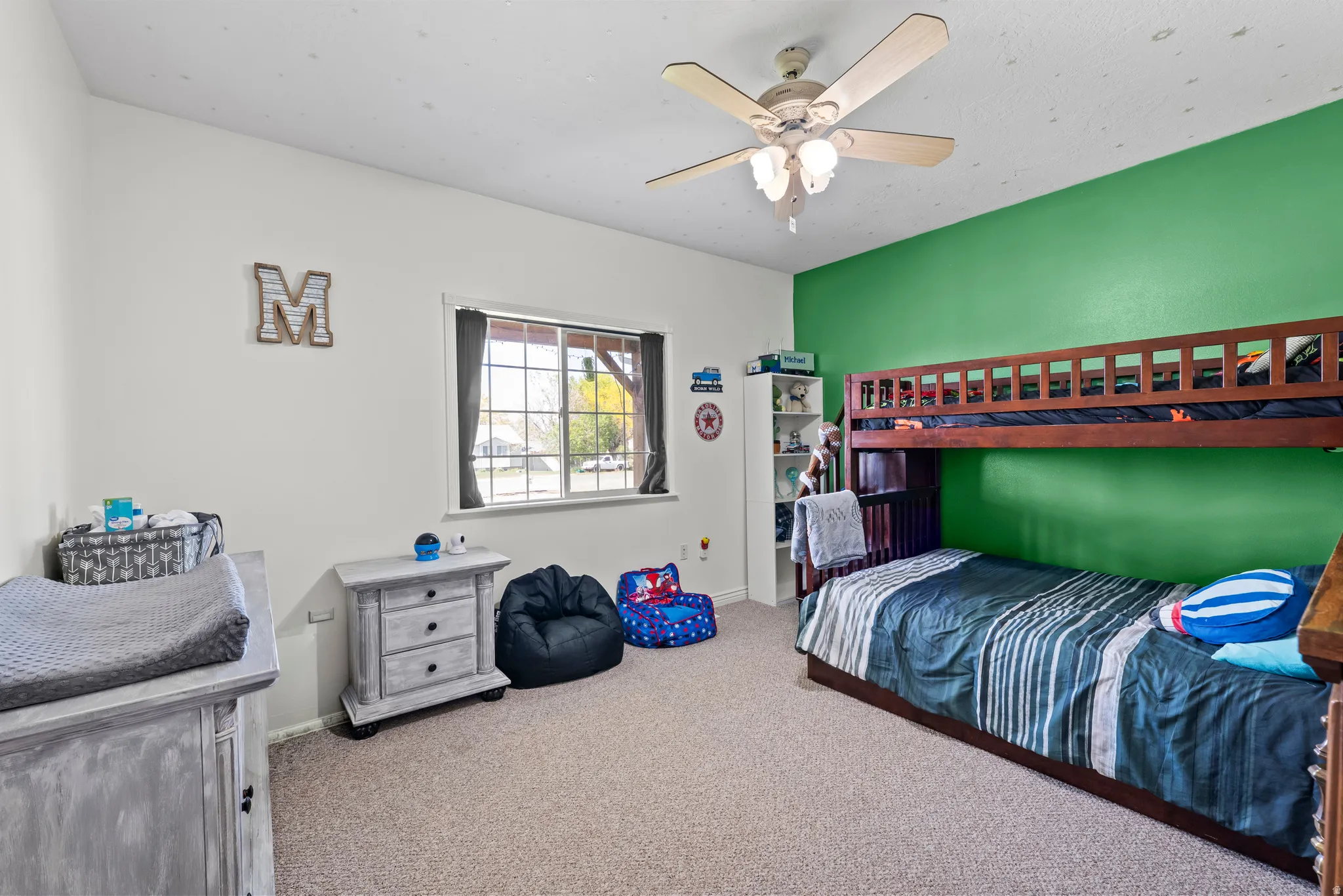 Carpeted room featuring a ceiling fan with integrated lighting, a window with dark drapes, and a vibrant green accent wall