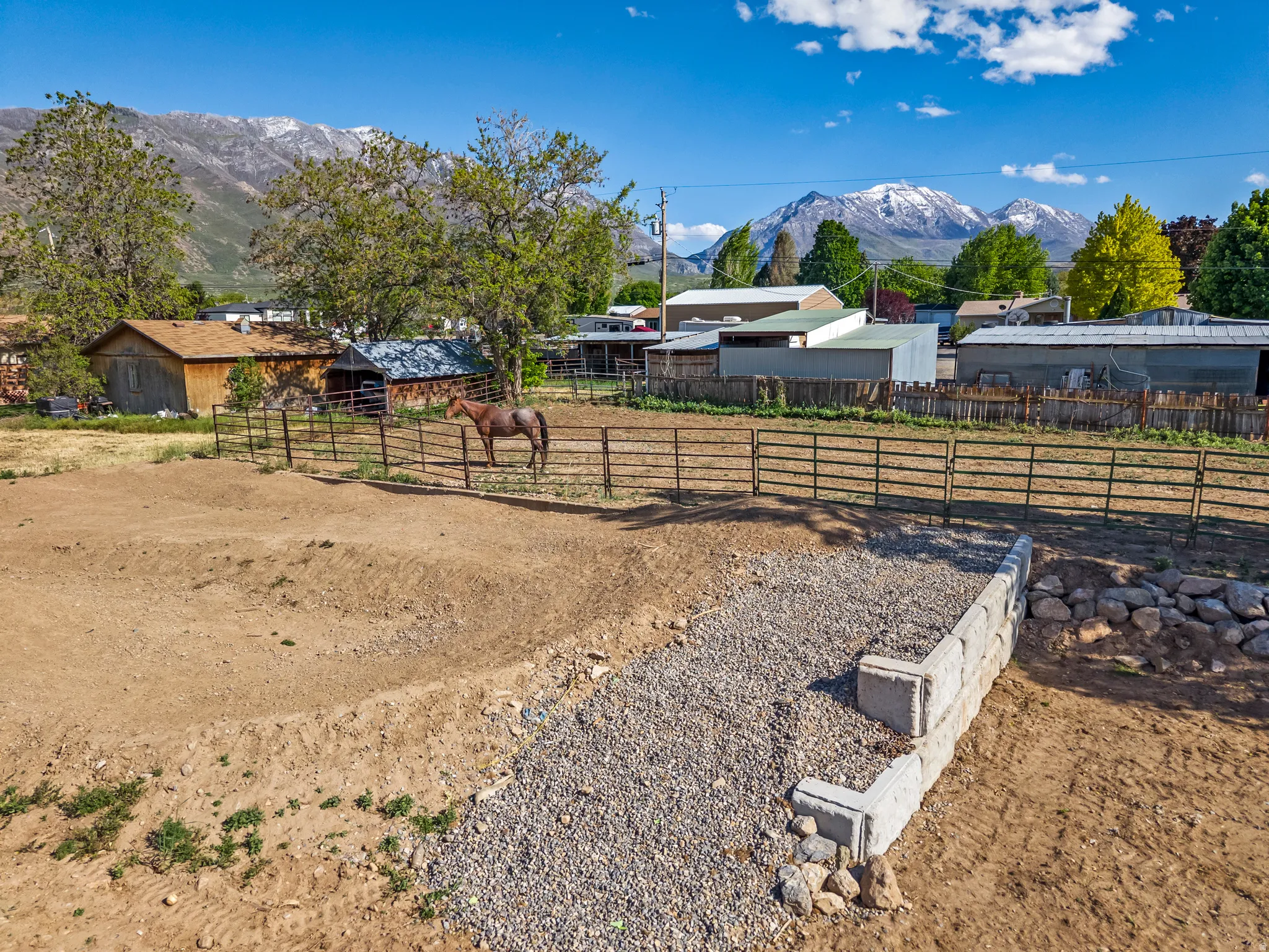 Expansive property featuring a cleared land area, a retaining wall with gravel, and a fenced enclosure