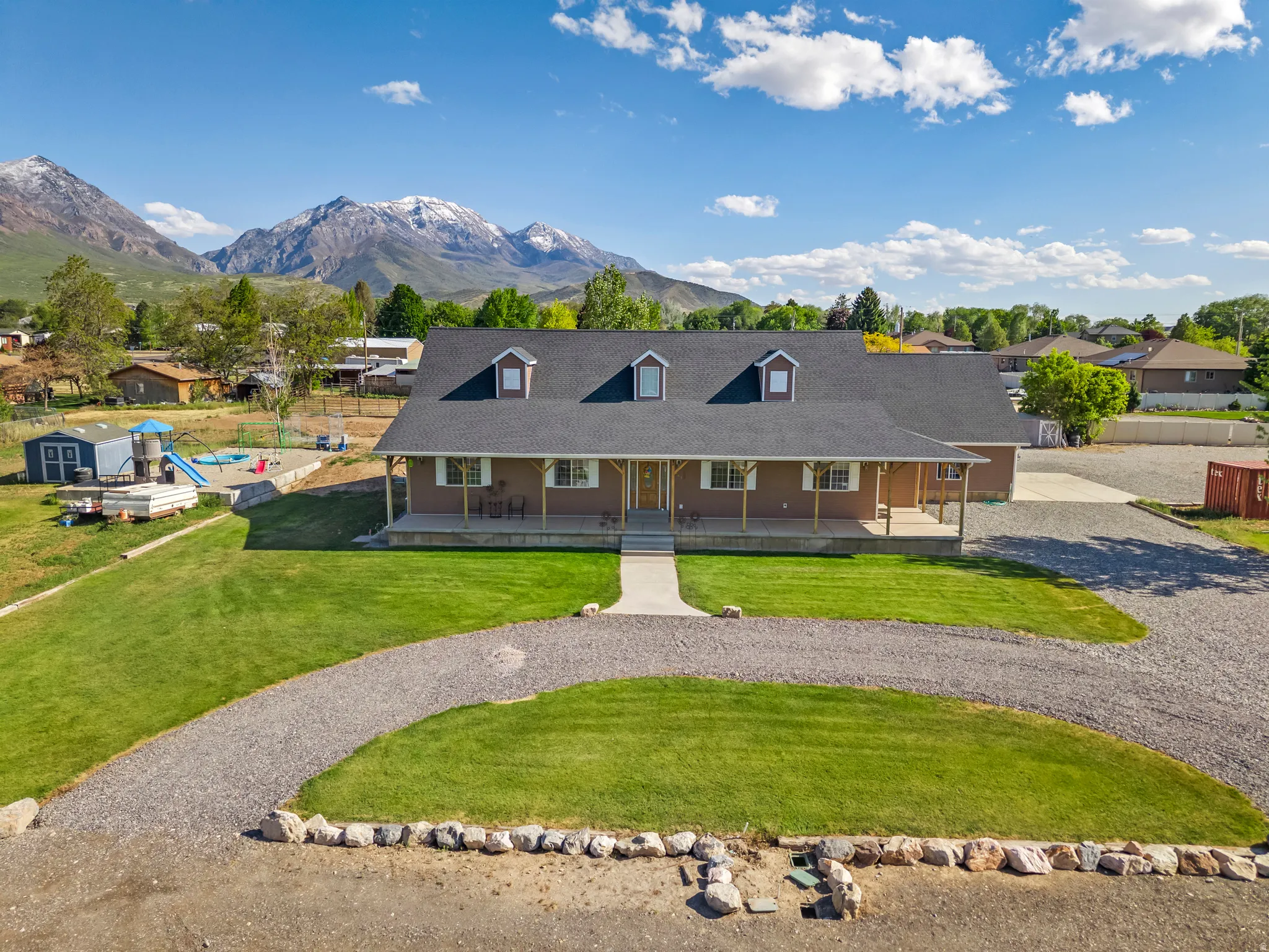 Ranch-style residence featuring a covered front porch, dormer windows, and a gravel driveway