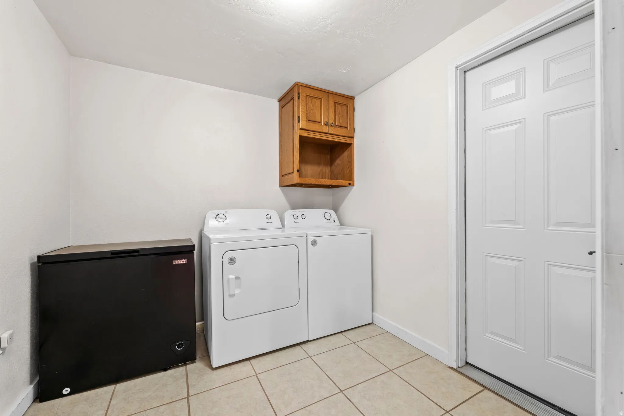 Laundry area featuring neutral-toned tile flooring, light wall paint, and a wood-finish wall cabinet