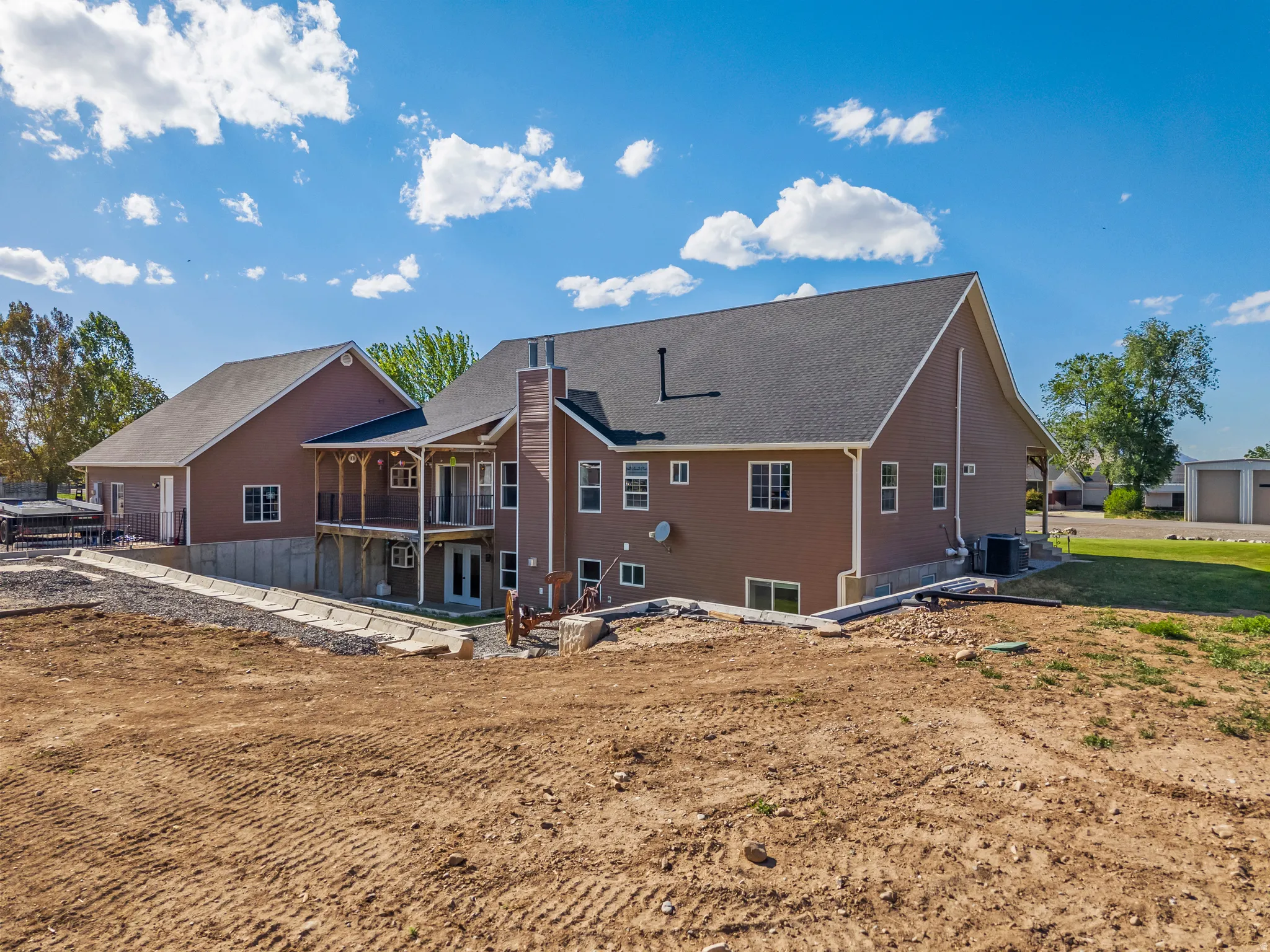 Rear exterior featuring a covered deck with white railing, double French doors, and a ground-level patio