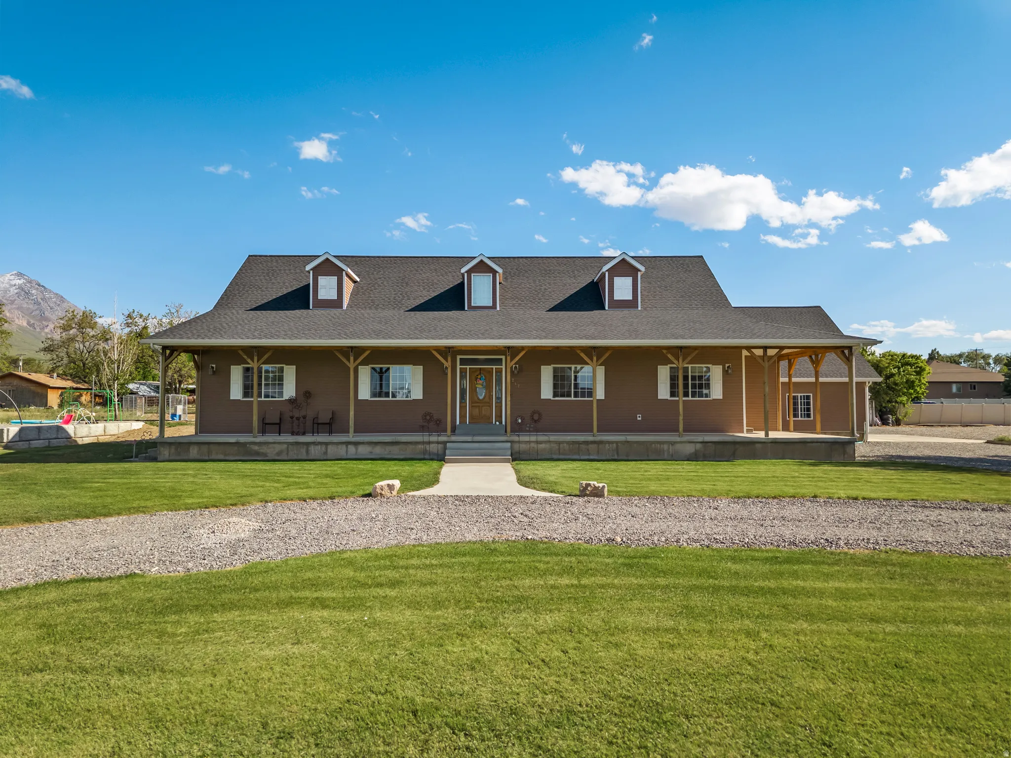 Ranch-style residence featuring a broad front porch with exposed wooden pillars, a dark shingle roof, and three dormer windows