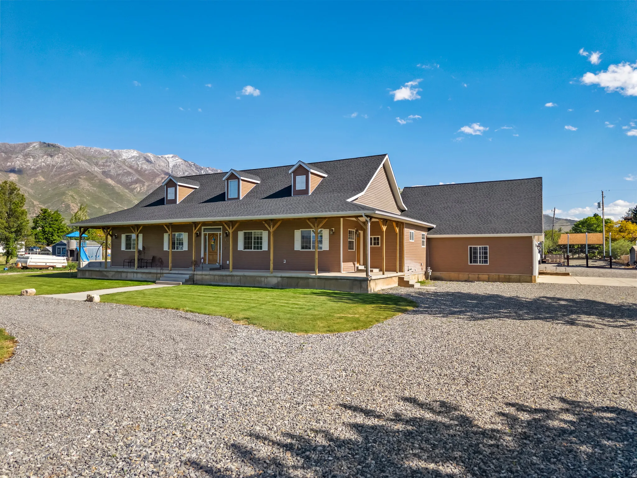 Expansive main residence with a covered front porch, dormer windows, and a detached two-story structure, all set against a mountain backdrop