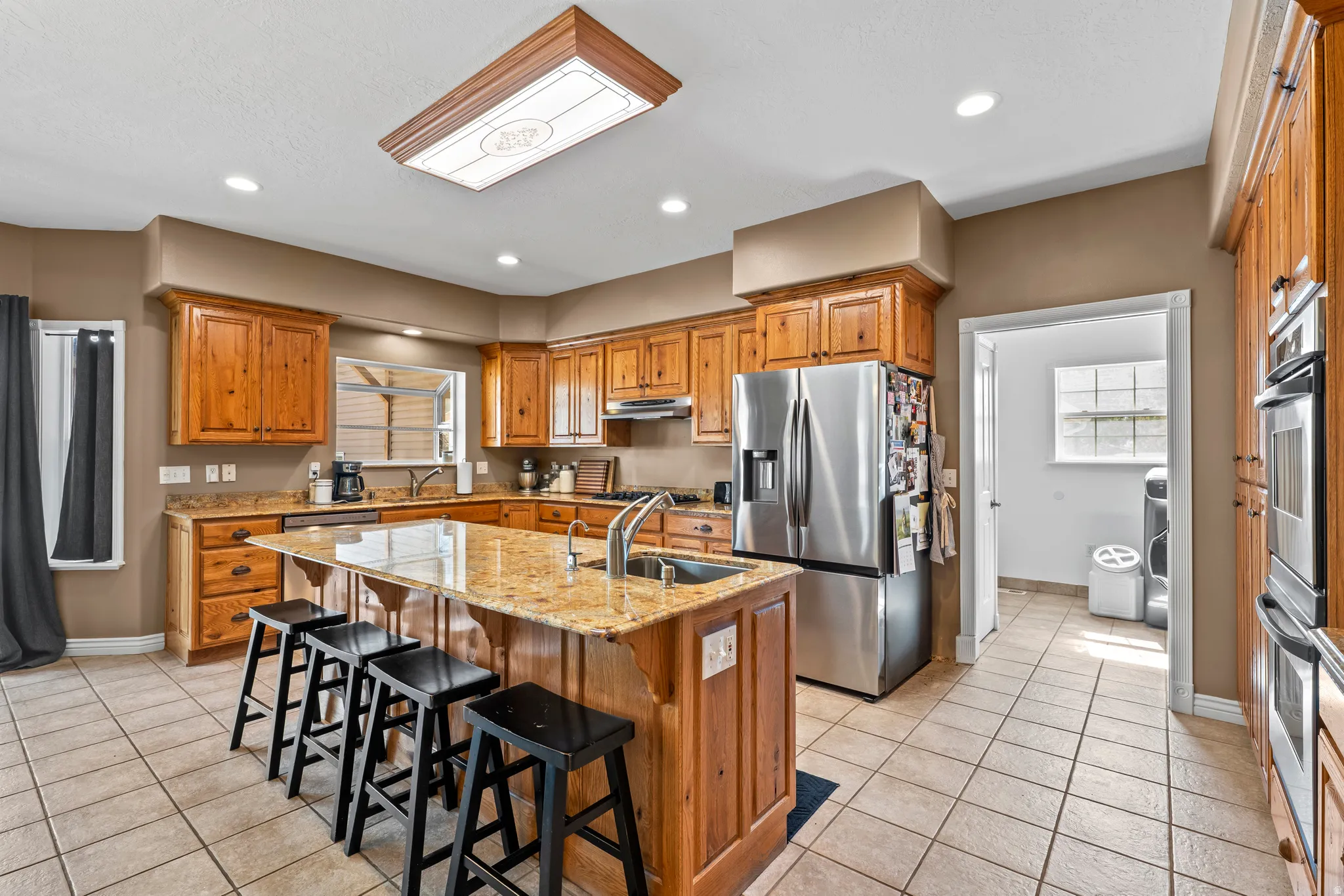 Kitchen featuring a large central island with a sink, wood cabinetry, stainless steel appliances, recessed lighting, and tile flooring