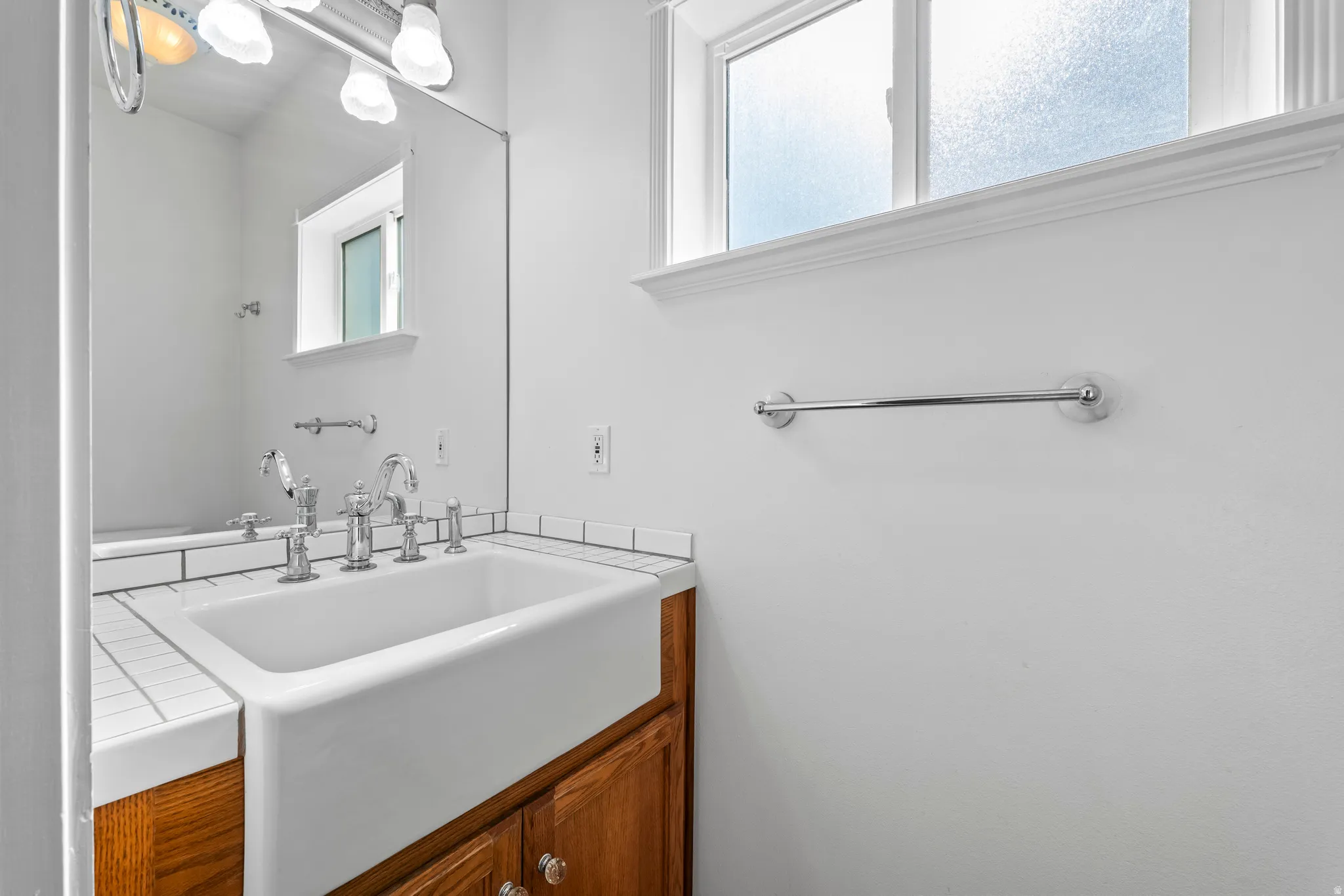 Bathroom featuring a deep apron-front sink, polished chrome fixtures, white subway tile countertop, and a wood-finish vanity