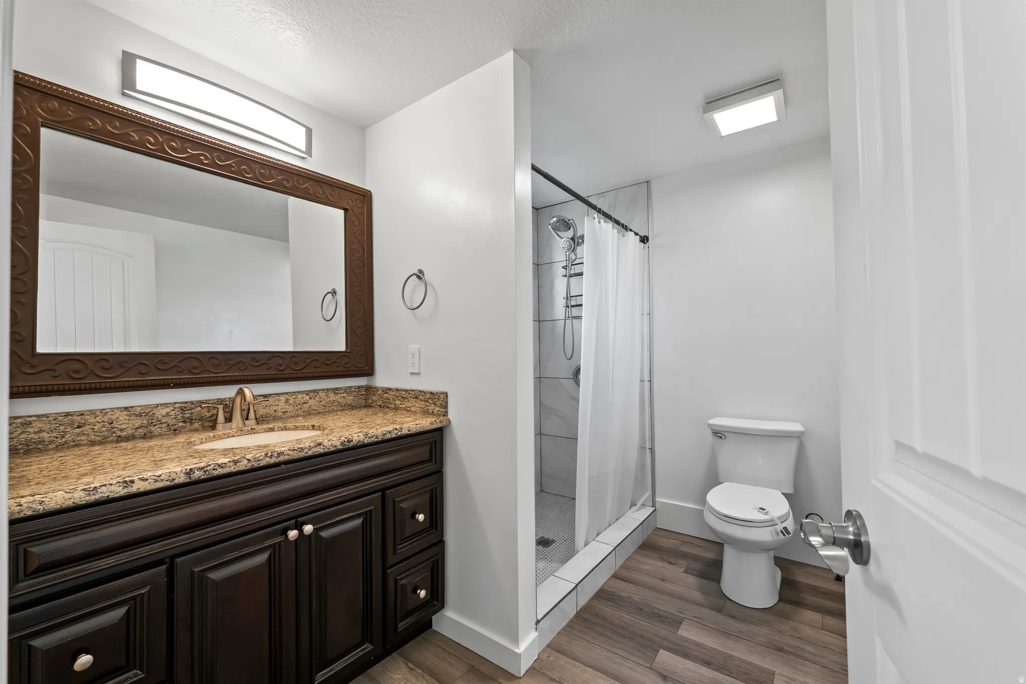 Bathroom featuring a dark wood-finish vanity with a light-colored countertop, an ornate framed mirror, and a walk-in shower with tiled walls