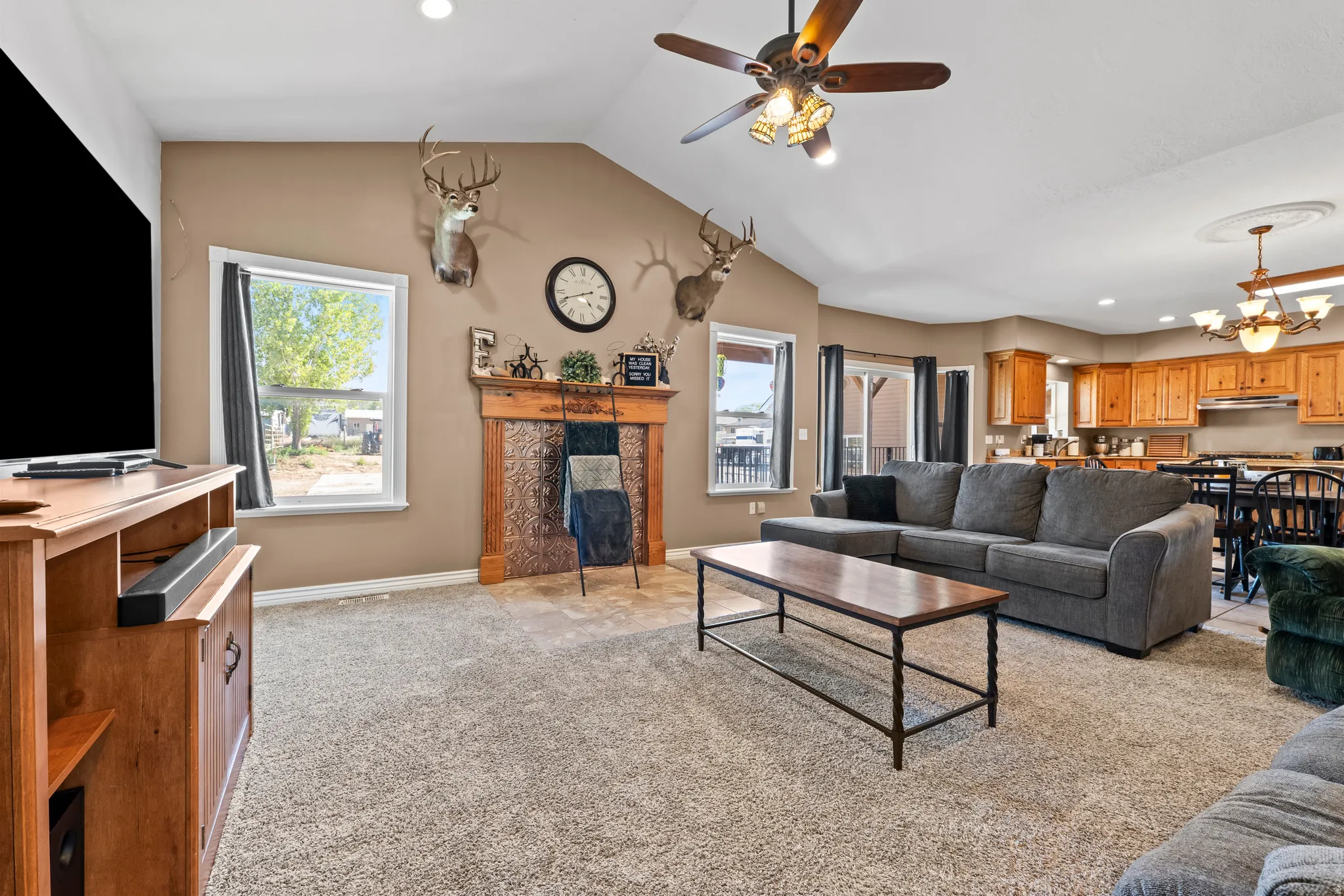 Spacious living area featuring vaulted ceilings, a ceiling fan with integrated lighting, and carpeted flooring