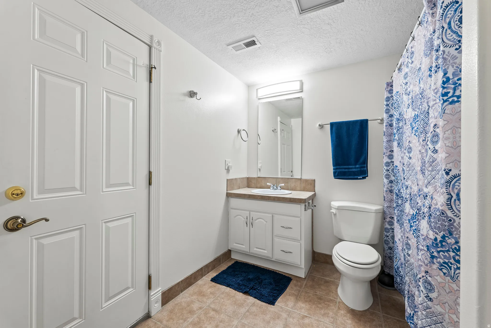 Full bathroom featuring a white vanity with integrated sink, a light-toned countertop, and tile flooring