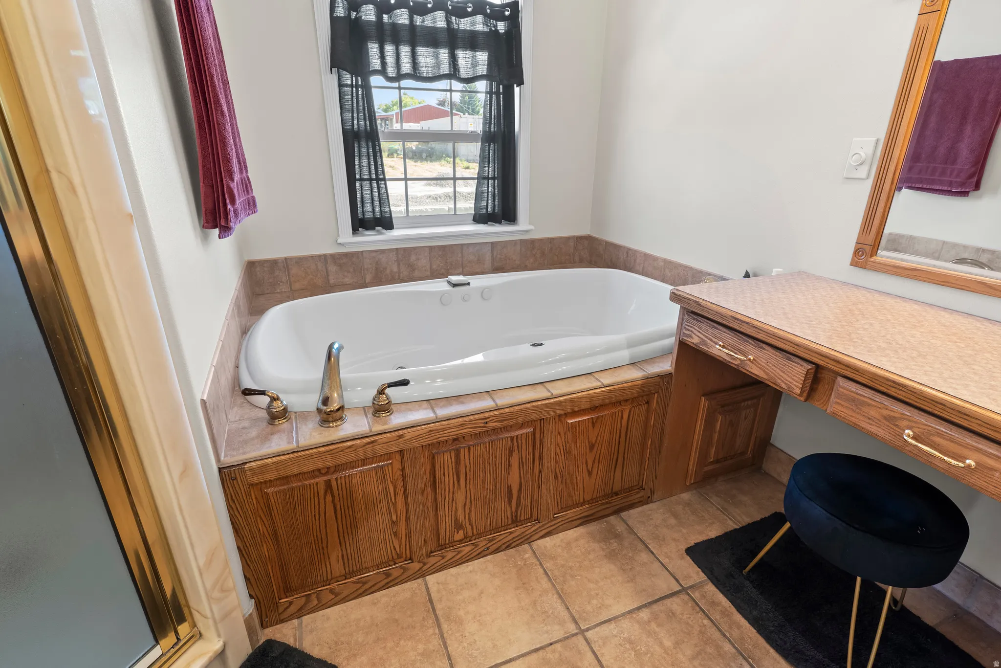 Soaking tub with tiled surround, wood-finish paneling, and polished chrome fixtures