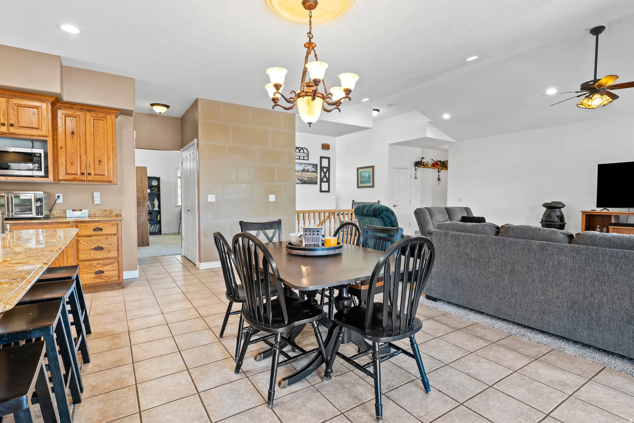 Open-concept living area featuring a kitchen island with seating, a dining area with chandelier lighting, and a living room with vaulted ceilings and a ceiling fan