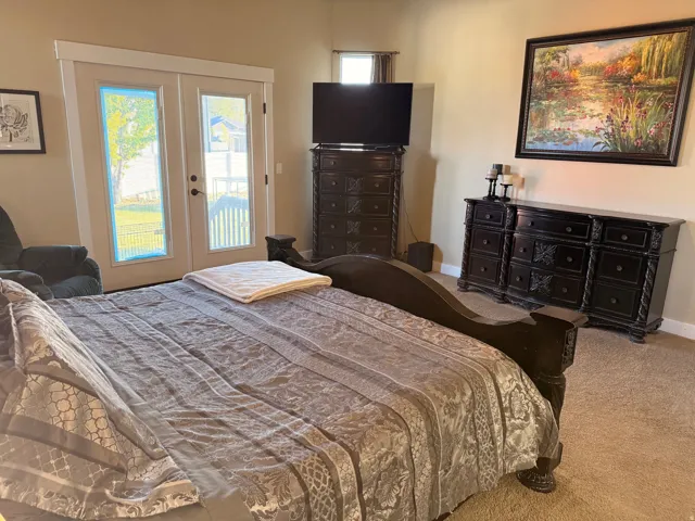 Master bedroom carpeted interior space featuring light beige walls and a double French door entry with white trim
