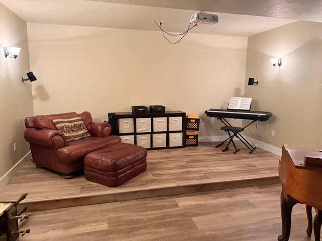 Theatre room with raised platform area featuring wood-finish flooring, recessed lighting, and a ceiling-mounted projector