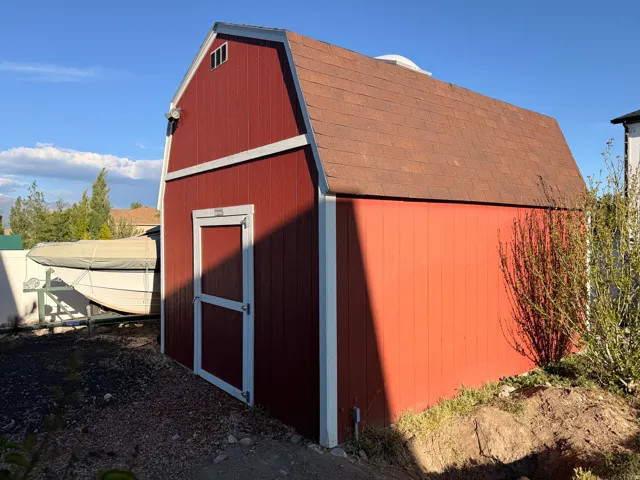 Red board-and-batten style shed with white trim, a brown shingled gambrel roof, and a single entry door