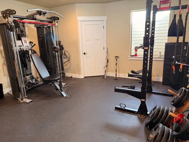 Dedicated fitness space featuring impact-absorbing flooring, neutral wall tones, a modern three-panel interior door, and a prominent window with privacy blinds