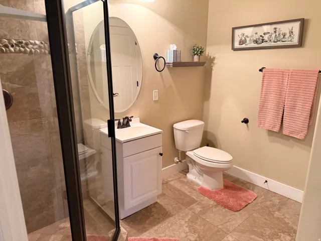 Walk-in shower with glass enclosure and pebble accent tile, complementing the vanity with an oval mirror