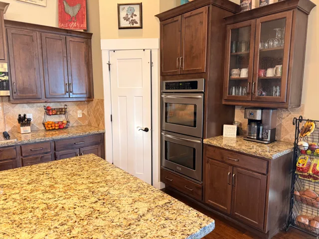 Kitchen featuring extensive cabinetry in a rich wood tone, granite countertops, a built-in stainless steel double oven, and a tiled backsplash