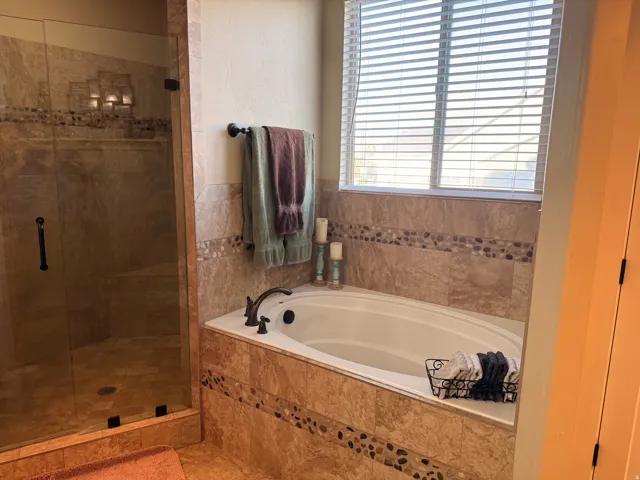 Master bath with soaking tub and enclosed shower featuring a glass door, tile surround, stone accent band, and dark bronze fixtures