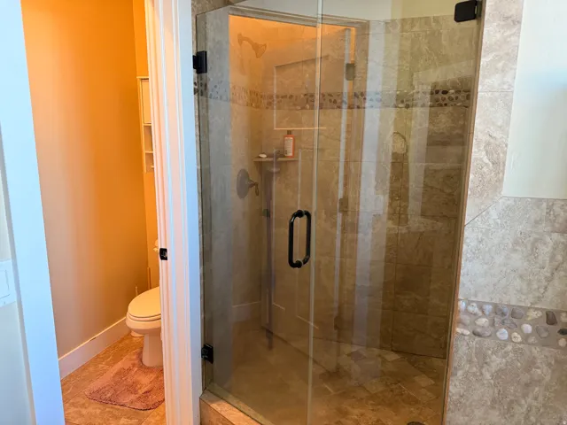 Master bathroom with glass-enclosed shower featuring large format tile, pebble tile accent band, and a built-in shower niche