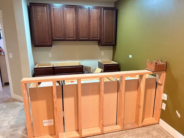 Partially finished wet bar with custom cabinetry installation featuring upper dark wood-finish cabinets and base cabinet frames