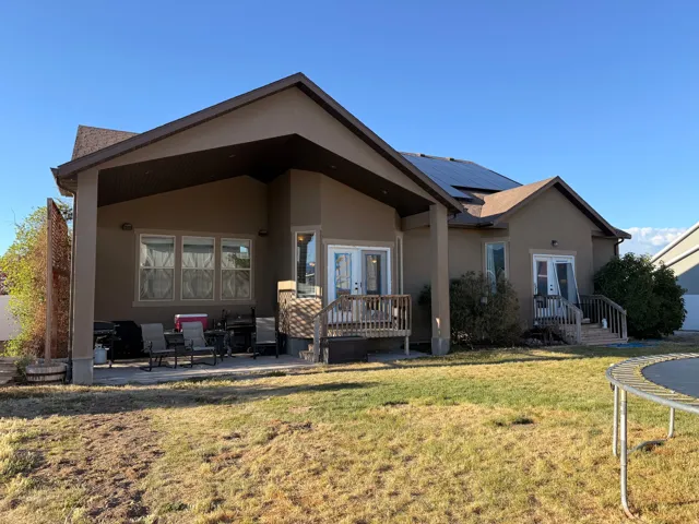 Rear exterior featuring a covered patio, multiple entry points, and a pitched shingle roof with integrated solar panels