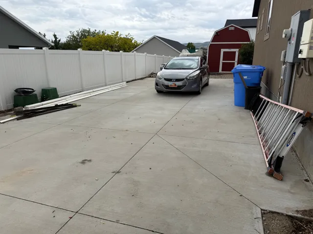 Expansive concrete driveway with a durable white vinyl fence, storage shed.