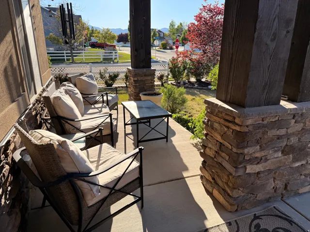 Inviting covered porch featuring stone-clad pillars, wood-finish columns, a concrete floor, and exterior siding