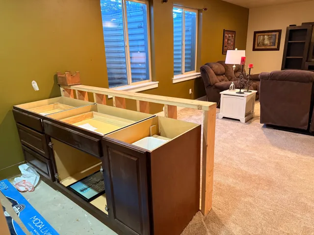 Wet bar featuring a partial cabinet installation, neutral tone carpeting, and two egress windows
