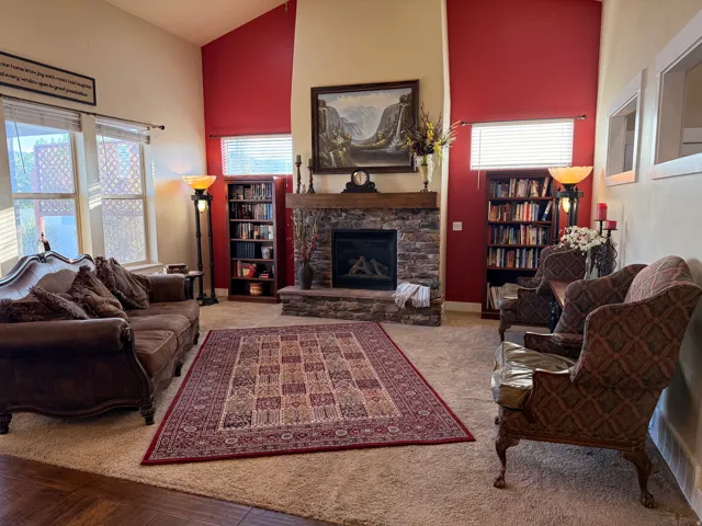 Living area featuring a stone-clad fireplace with wood mantel, vaulted ceilings, and integrated shelving