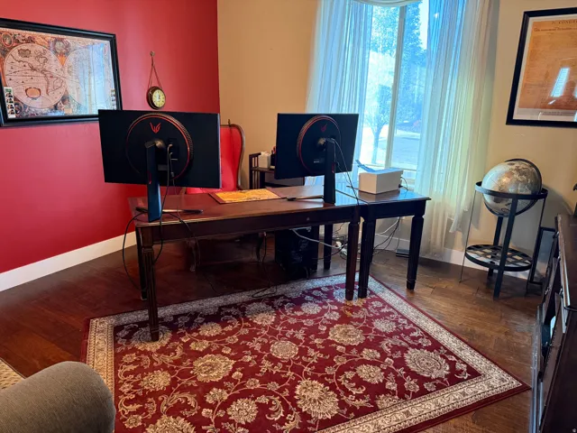 Office space featuring wood-finish flooring, a large window with sheer drapes, and a vibrant accent wall