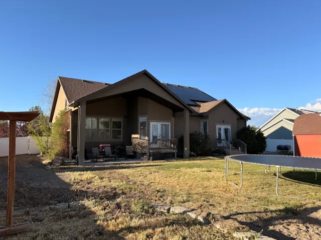 Rear exterior featuring a covered patio, multiple egress points, solar panels, and a brown shingle roof
