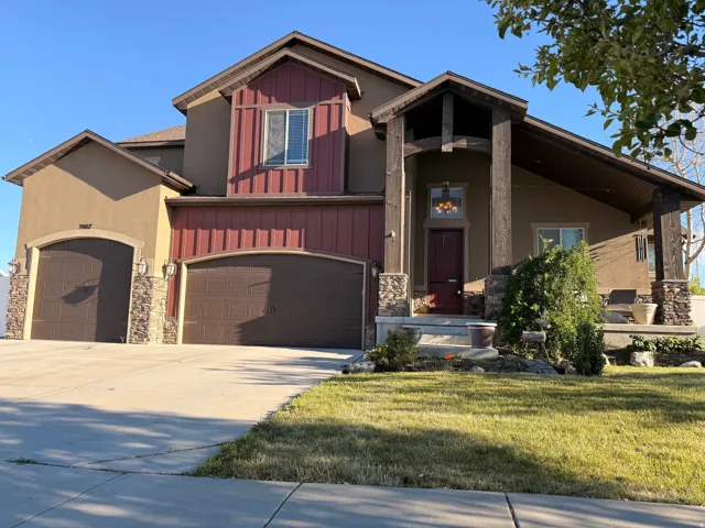 Stucco and board-and-batten exterior with a covered entry, stone accents, two arched garage doors, and a concrete driveway