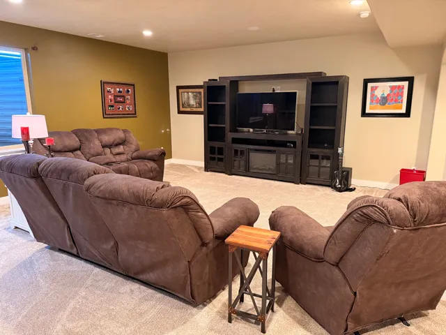 Carpeted recreation room featuring recessed lighting, a window with horizontal blinds, and a built-in media console with shelving