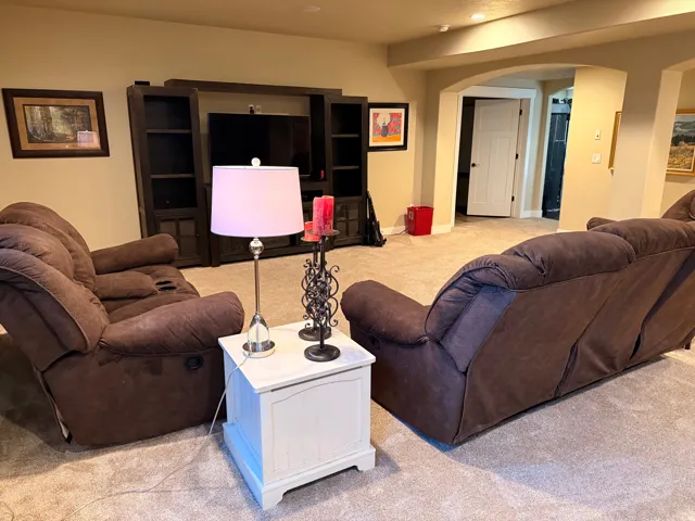 Carpeted living area featuring a built-in entertainment center with open shelving, recessed lighting, and an arched doorway