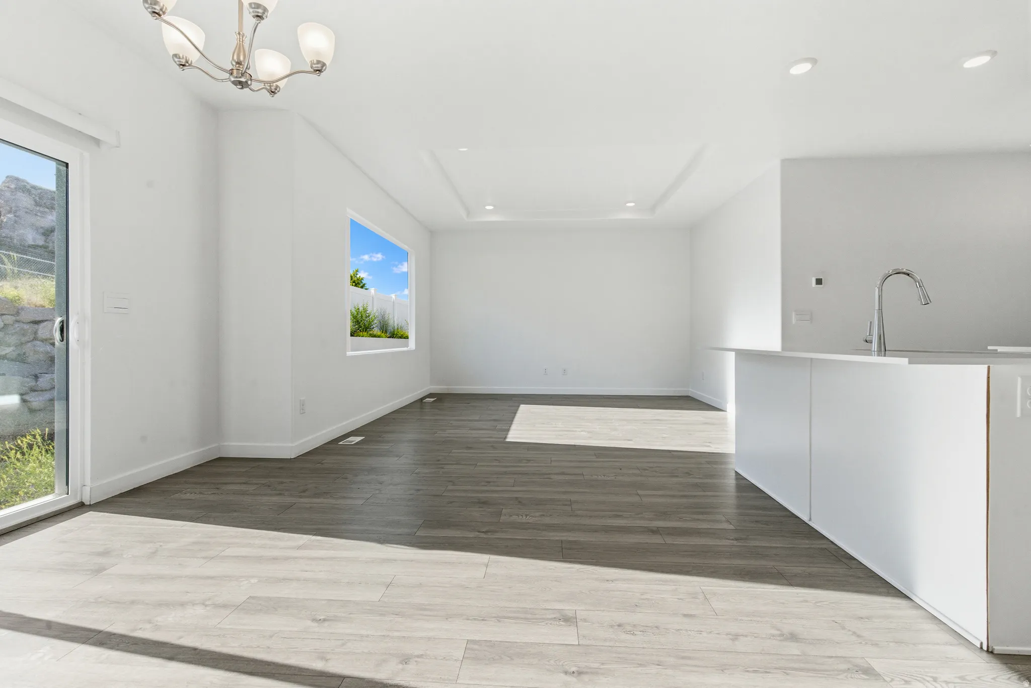 Open-concept living space featuring wood-finish flooring, a contemporary island with a gooseneck faucet, a sliding glass door, and a recessed ceiling detail